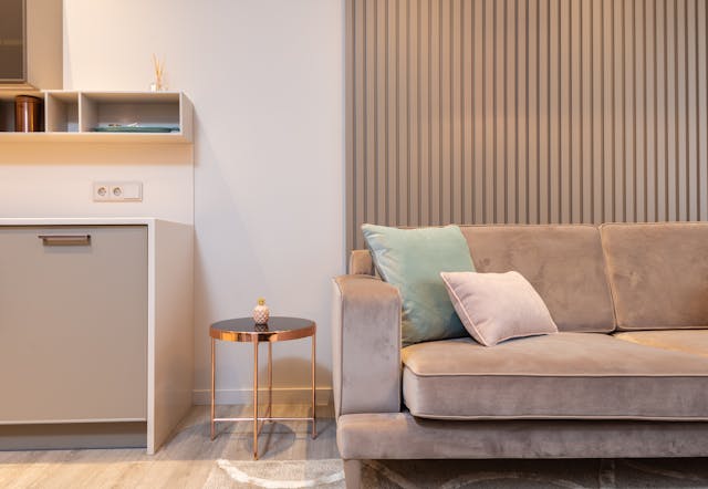 light-brown-couch-with-two-throw-pillows-on-it-beside-a-side-table